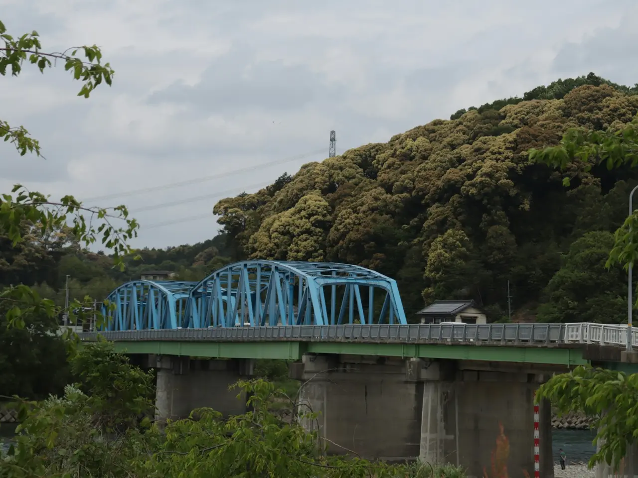 山を背にして川にかかる、水色の鉄のトラス橋